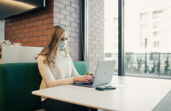 Student with mask on computer by window