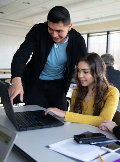 student helping a peer on her laptop