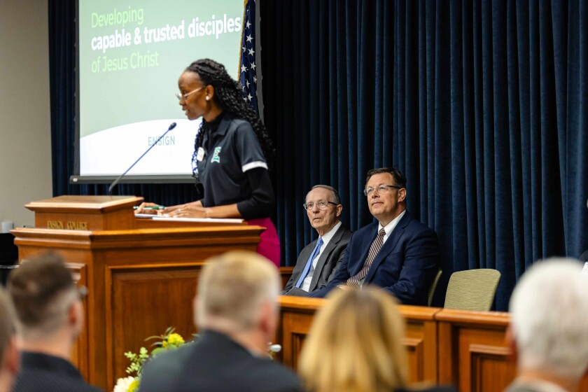 Schekina Boumba speaks at a podium while Elder Clark G. Gilbert and President Bruce C. Kusch sit on the stand behind her.