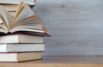 Stack of books on the left of a table with a wooden background